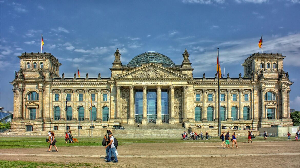 Front view of the Reichstag Building in Berlin with people and flags, under a bright sky.