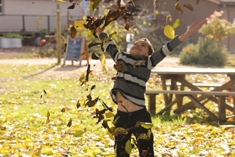 Fröhliches Kind wirft Blätter an einem sonnigen Herbsttag im Park