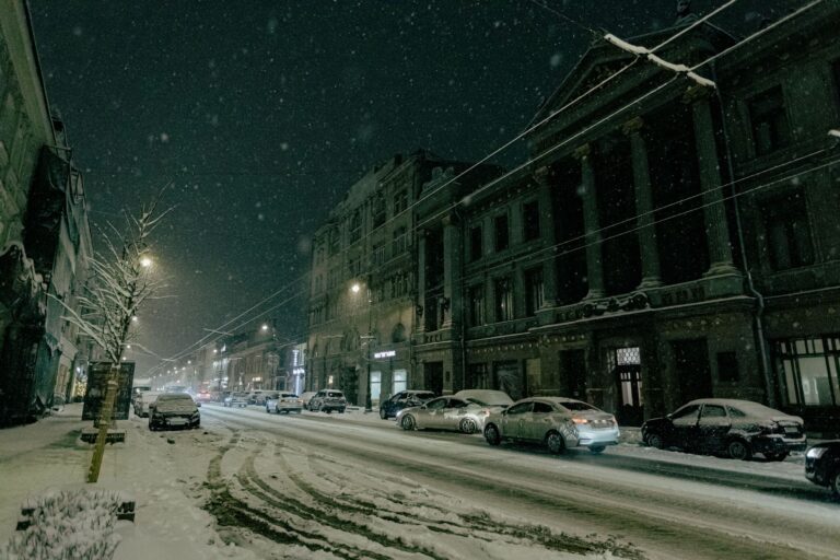 Schneebedeckte ruhige Straße mit geparkten Autos und historischen Gebäuden bei Nacht