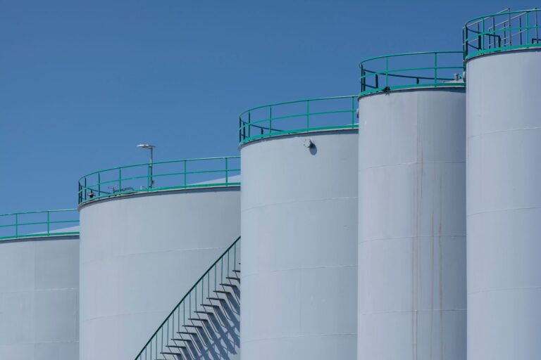 Große industrielle Lagertanks mit grünen Geländern vor blauem Himmel
