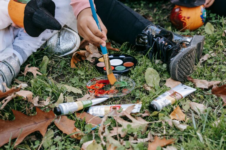 Kinder malen mit Wasserfarben und Pinseln auf dem Boden mit Herbstlaub